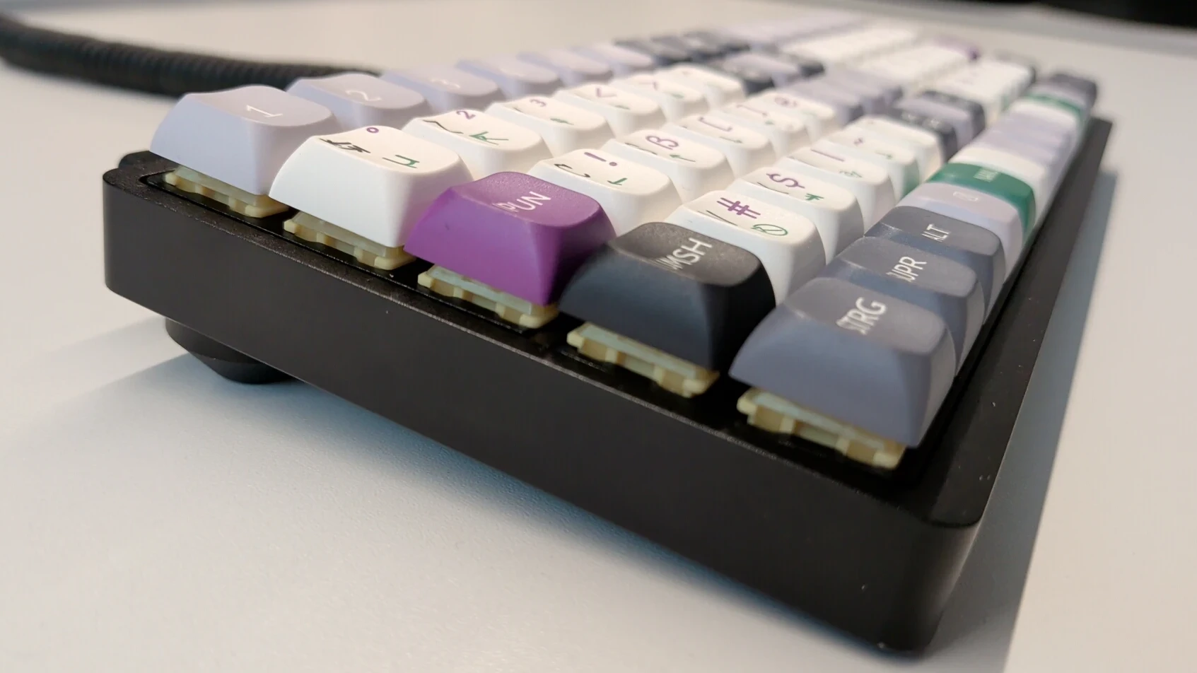 15x5 ortholinear keyboard with the Firmlynoted layout, black, purple, green and white labels. Shown from a front-left angle.